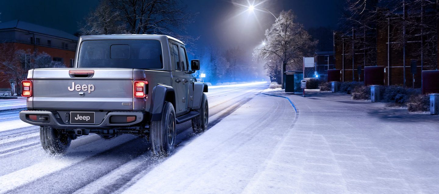 A rear view of a 2021 Jeep Gladiator Overland being driven on a snow-covered road at night.