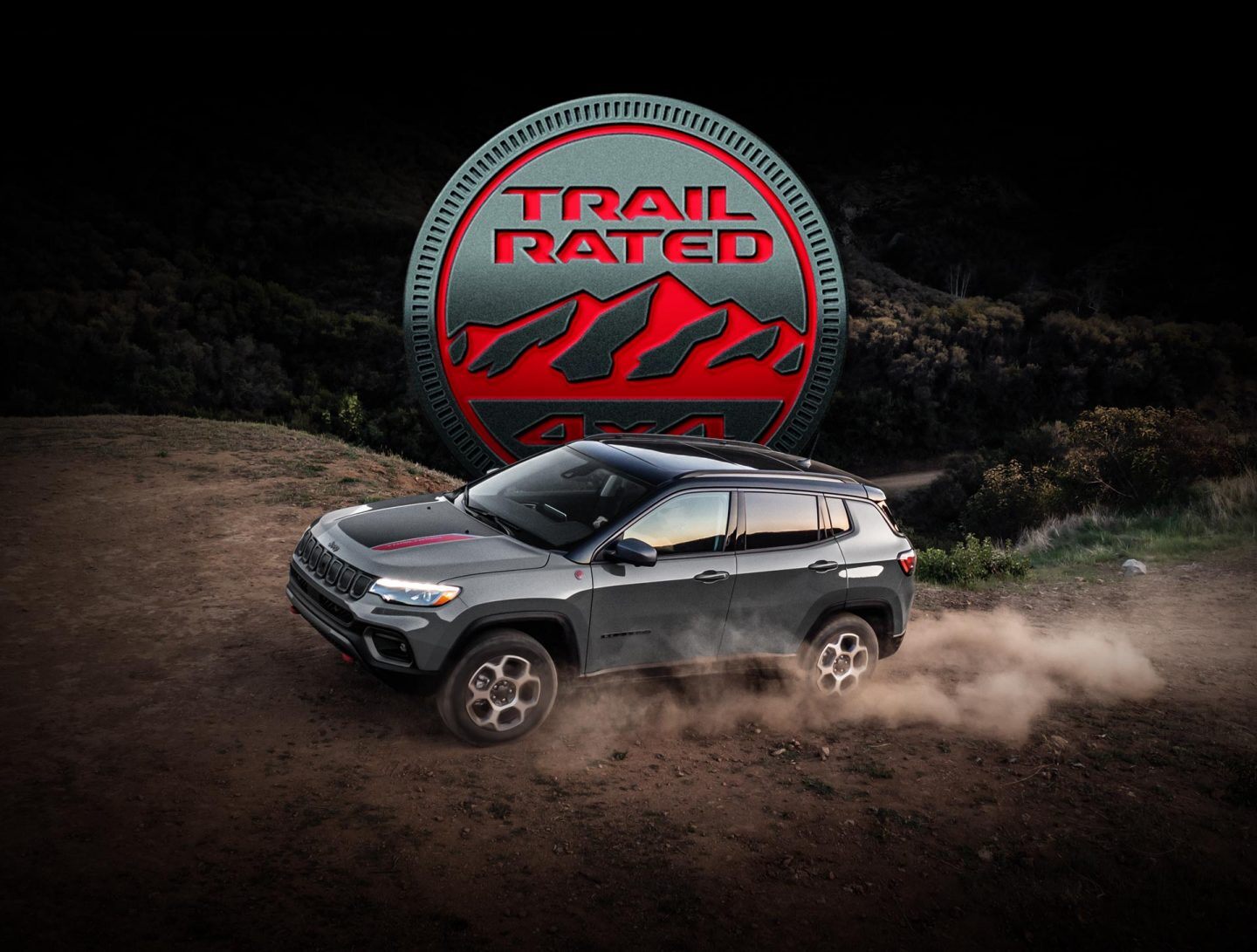 Trail Rated logo. The 2022 Jeep Compass Trailhawk being driven off-road on packed earth with dust rising from its wheels.