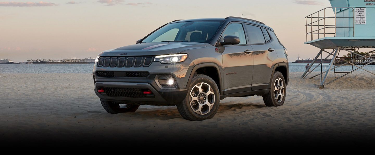 The 2022 Jeep Compass Trailhawk parked on a beach with tire tracks visible on the sand behind it.