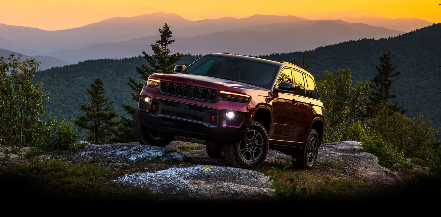 The 2022 Jeep Grand Cherokee Trailhawk being driven off-road, with both front wheels elevated as it is driven over rocks.