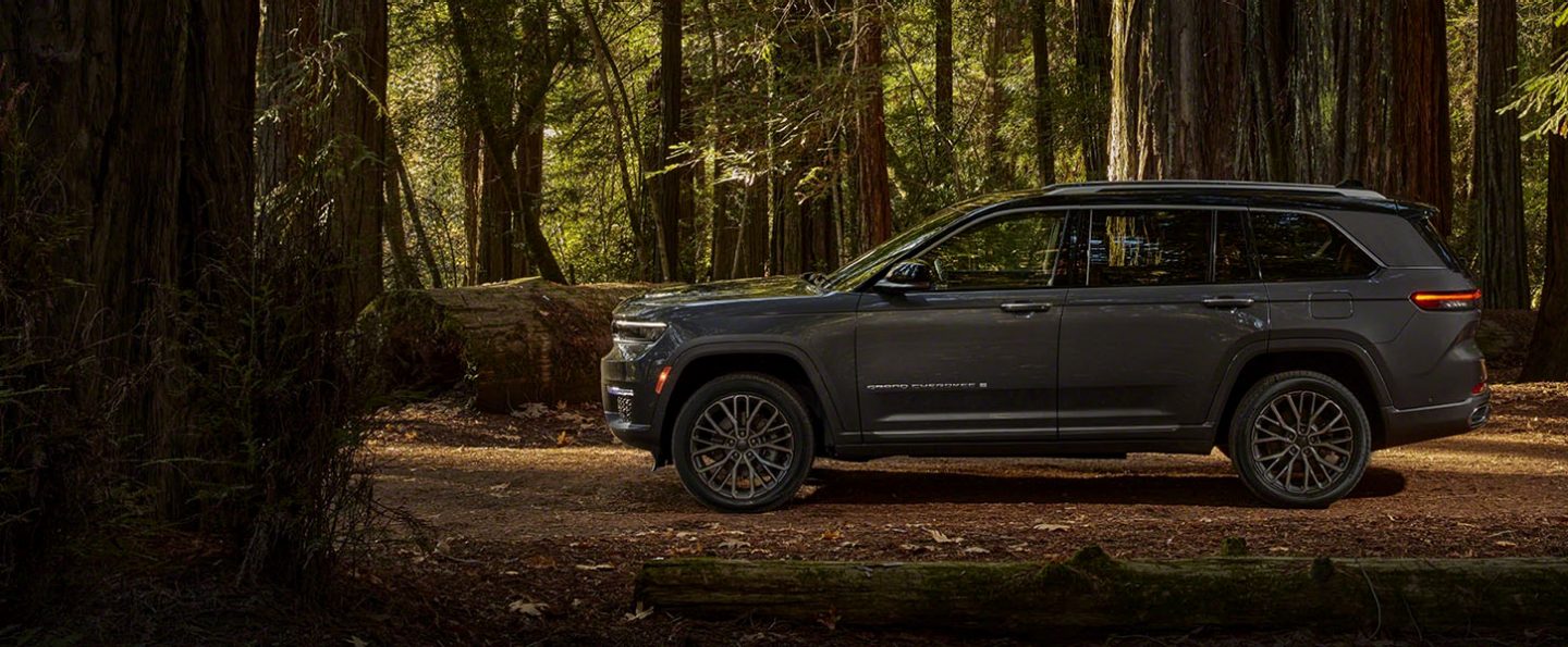 A side profile of the two-row 2022 Jeep Grand Cherokee Summit Reserve against a backdrop of trees, allowing the viewer to estimate its length.
